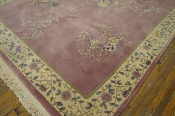Mauve floral rug with carved details, a cream border featuring vines and birds, laying on hardwood floors.