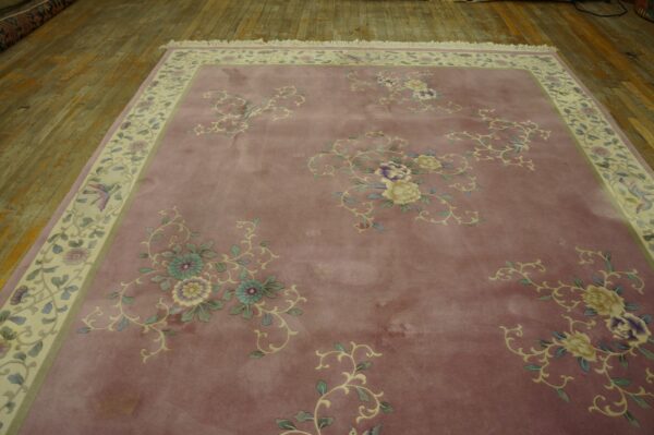 Mauve rug with scattered multicolored floral designs and a patterned cream border on distressed wooden floors.