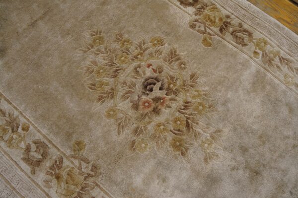 Close-up of a distressed beige and brown floral medallion rug, visible next to light wood flooring.