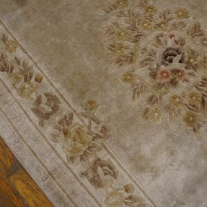 Close-up of a tan floral rug showing a distressed border and central medallion on wood flooring.