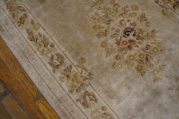Close-up of a tan floral rug showing a distressed border and central medallion on wood flooring.