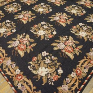 Dark blue rug with ornate repeating cream and rust floral bouquets rests on light, distressed wood flooring.