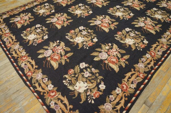 Dark blue rug with ornate repeating cream and rust floral bouquets rests on light, distressed wood flooring.