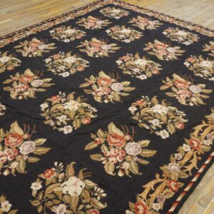 Black rug with allover floral bouquets and scrolling borders in gold, rose, and cream on wood floor.