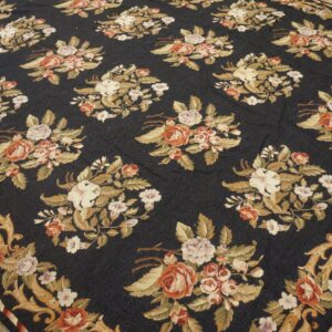 Navy floral rug with repeating bouquets in peach, cream, and tan, bordered by ornate scrolls on wood flooring.