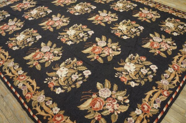 Navy floral rug with repeating bouquets in peach, cream, and tan, bordered by ornate scrolls on wood flooring.