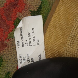 Hooked pile rug in olive, red, and green floral pattern, showing its woven backing and product label.