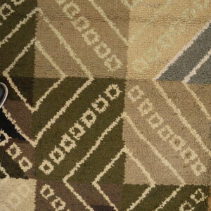 Dark green, brown, and tan geometric rug with high loop pile resting on a wood floor.