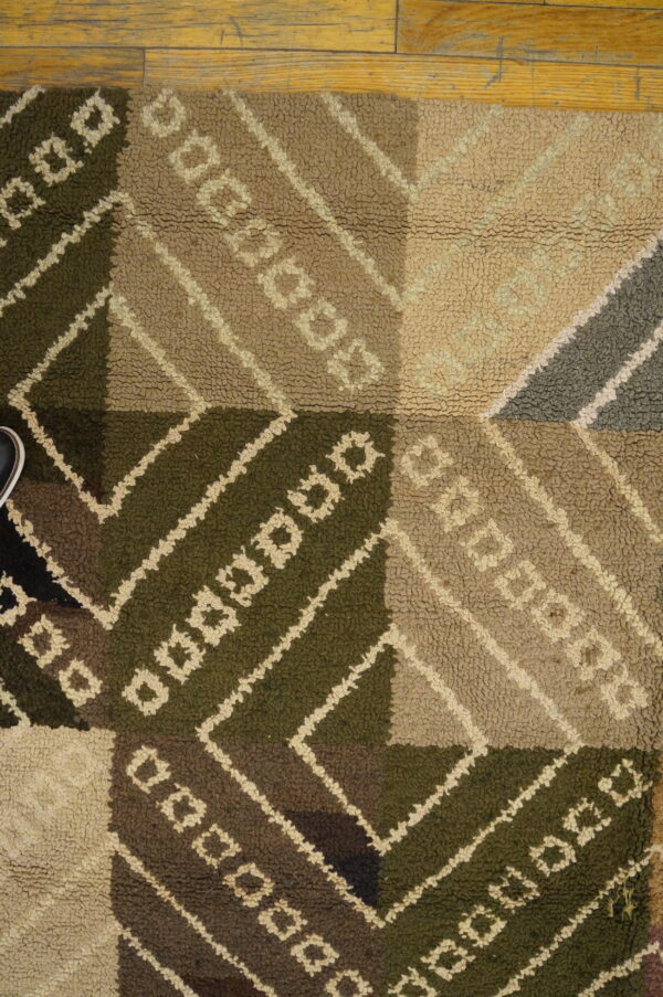 Dark green, brown, and tan geometric rug with high loop pile resting on a wood floor.