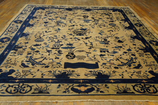 Tan rug with detailed indigo chinese floral and vase patterns on wide plank wood floors.