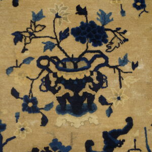 Low-pile rug detail featuring a stylized floral vase motif in navy and light blue on a tan ground.