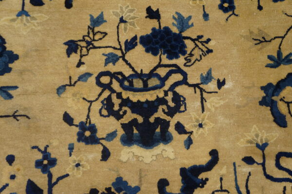 Low-pile rug detail featuring a stylized floral vase motif in navy and light blue on a tan ground.