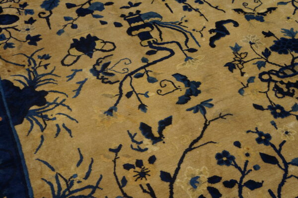 Gold rug detail with sprawling dark blue floral and vine designs and a dark border.