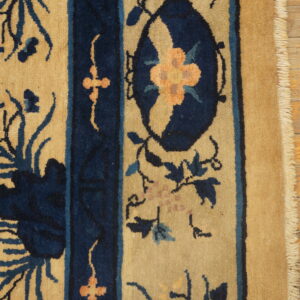 Tan and navy high-pile rug detail features stylized vines and an apricot floral medallion near the visible fringe.