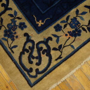 High-pile rug corner featuring navy blue floral motifs on a tan ground, resting on rustic hardwood floors.