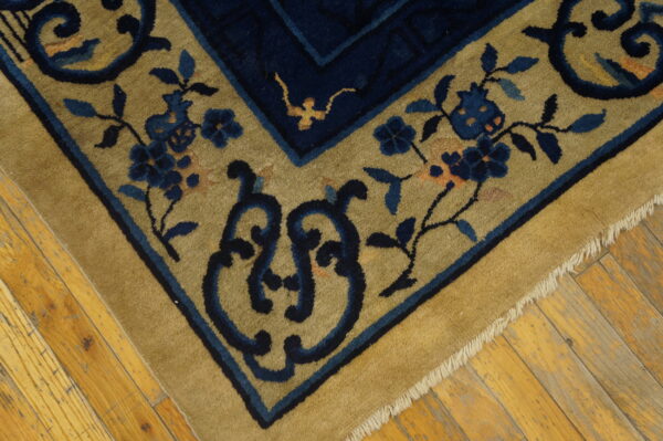 High-pile rug corner featuring navy blue floral motifs on a tan ground, resting on rustic hardwood floors.