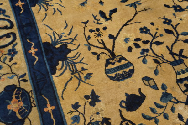 Tan field rug featuring a dark blue border and intricate botanical and object motifs.