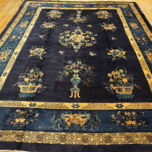 Dark blue rug featuring elaborate gold and light blue vases, flowers, and multiple traditional borders on wood.