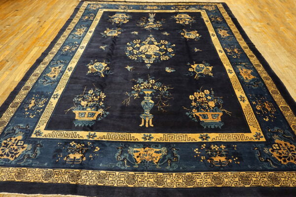Dark blue rug featuring elaborate gold and light blue vases, flowers, and multiple traditional borders on wood.