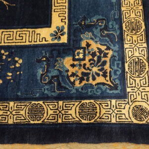 A deep blue rug featuring tan borders with geometric patterns and stylized floral designs on wood flooring.