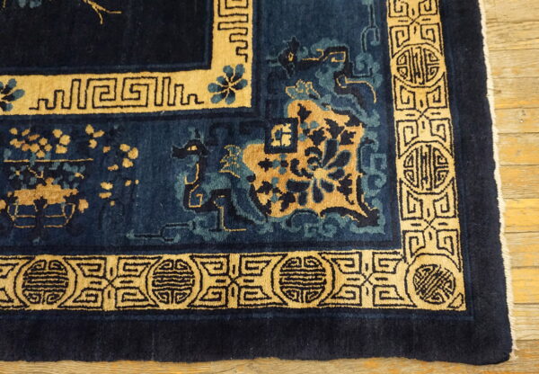 A deep blue rug featuring tan borders with geometric patterns and stylized floral designs on wood flooring.