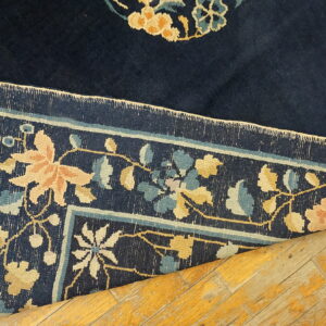 Navy floral rug with peach, gold, and blue motifs is folded over distressed, yellow wood planks.