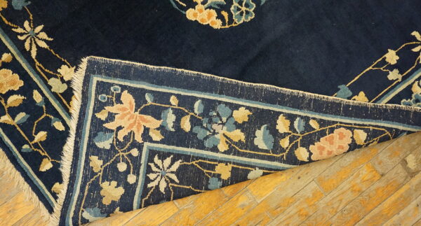 Navy floral rug with peach, gold, and blue motifs is folded over distressed, yellow wood planks.