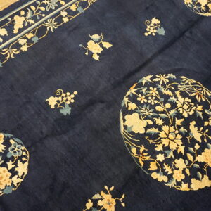 Navy rug with pale yellow floral medallions and a continuous border rests on light wooden floorboards.