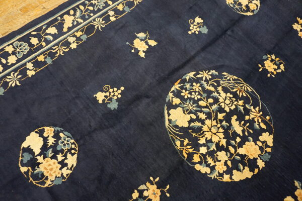 Navy rug with pale yellow floral medallions and a continuous border rests on light wooden floorboards.