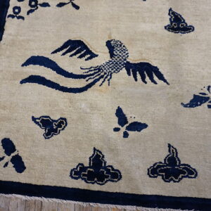 Light beige rug featuring dark blue phoenix and cloud motifs with a matching border on distressed wood floor.