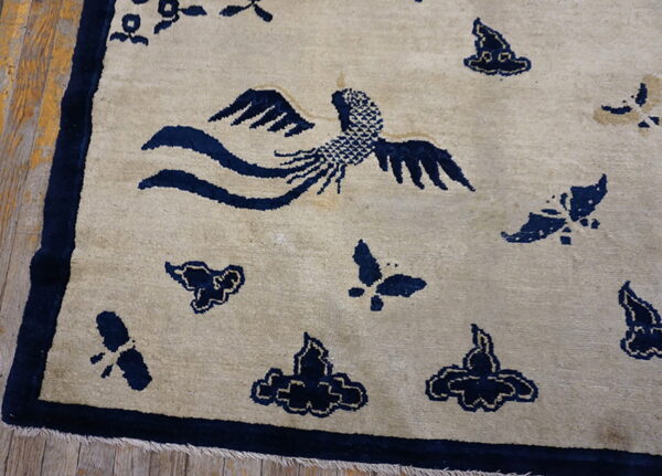 Light beige rug featuring dark blue phoenix and cloud motifs with a matching border on distressed wood floor.