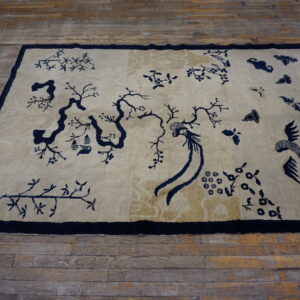 A rectangular beige rug features a bold navy blue chinoiserie pattern of trees, branches, and stylized birds.