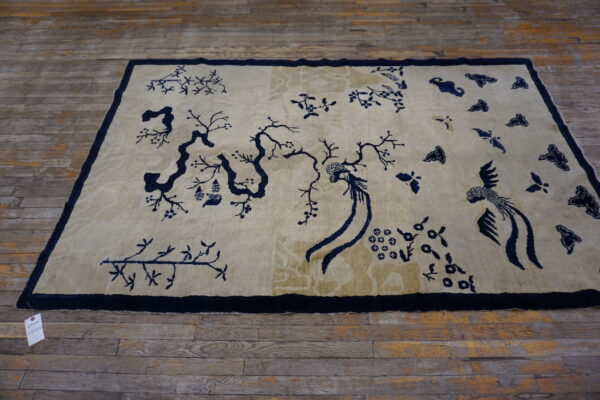 A rectangular beige rug features a bold navy blue chinoiserie pattern of trees, branches, and stylized birds.