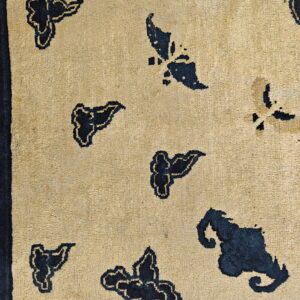 Tan rug detail showing a scattered pattern of navy blue motifs, framed by a dark blue border.