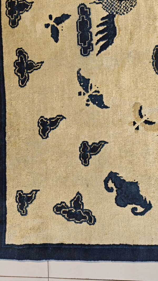 Tan rug detail showing a scattered pattern of navy blue motifs, framed by a dark blue border.