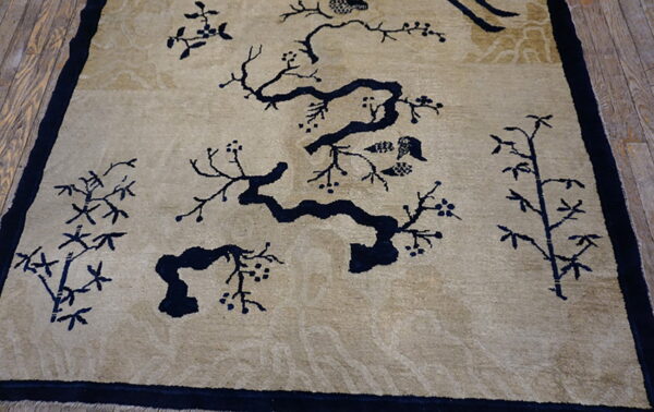 Beige rug with a dark blue scenic pattern of flowering branches and bamboo on wood flooring.