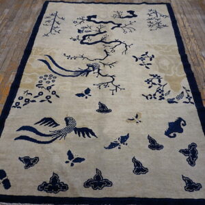 Tan rug with dark blue floral and bird motifs placed on rustic, narrow wooden planks.