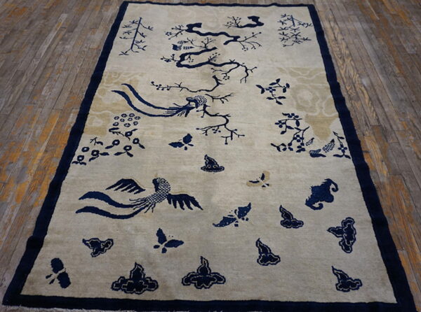 Tan rug with dark blue floral and bird motifs placed on rustic, narrow wooden planks.