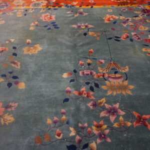 Teal plush rug with sprawling pink, purple, and gold floral designs and a vibrant reddish-orange border.