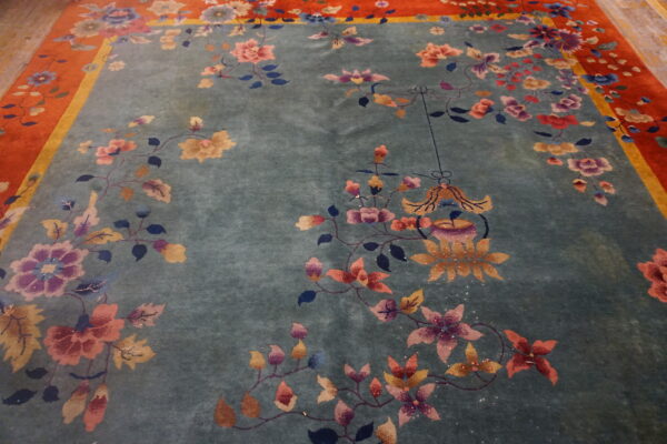 Teal plush rug with sprawling pink, purple, and gold floral designs and a vibrant reddish-orange border.