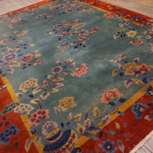 Floral rug featuring a teal center, multicolored flowers, and a broad rust-orange border on wood planks.