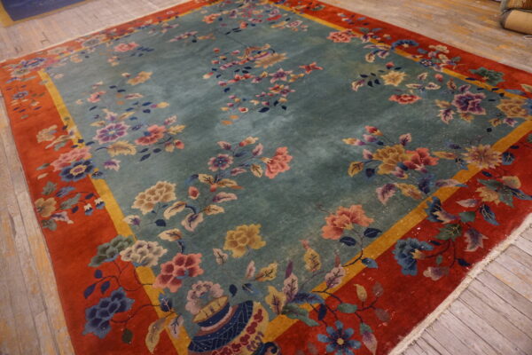 Floral rug featuring a teal center, multicolored flowers, and a broad rust-orange border on wood planks.