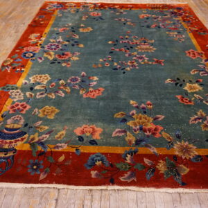 Teal floral rug with red and gold borders rests on light wood plank flooring.