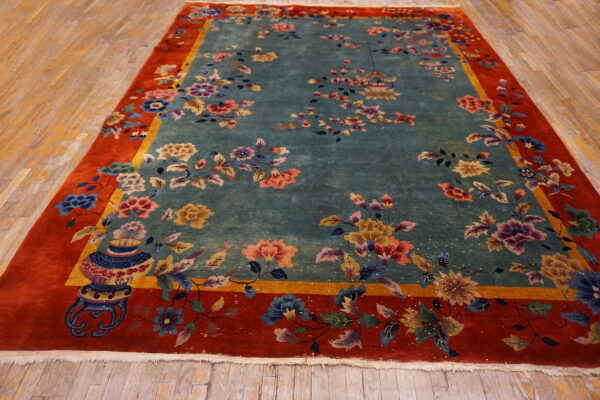 Teal floral rug with red and gold borders rests on light wood plank flooring.
