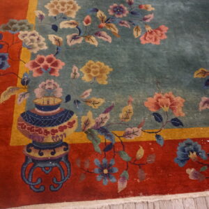 Detailed floral rug featuring a soft blue field, a vibrant red border, and a vase motif on wood flooring.
