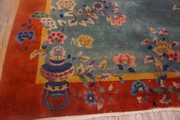 Detailed floral rug featuring a soft blue field, a vibrant red border, and a vase motif on wood flooring.