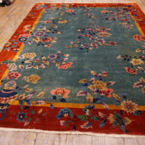 Vibrant floral rug featuring a teal center, wide red border, and visible vase motif on wood floors.
