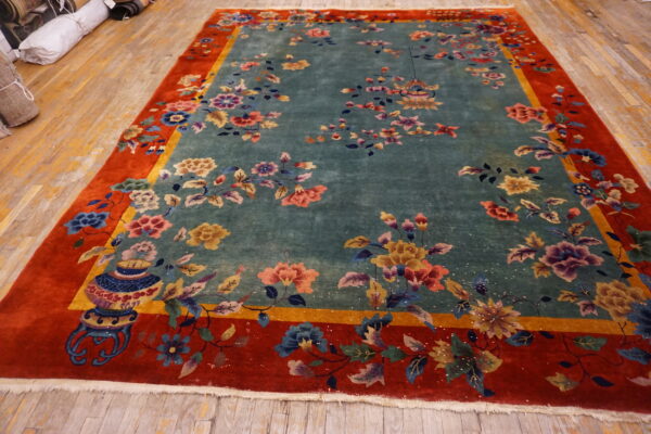 Vibrant floral rug featuring a teal center, wide red border, and visible vase motif on wood floors.