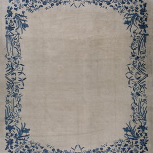 Low pile rug with a solid beige field and an elaborate blue floral and vine border.