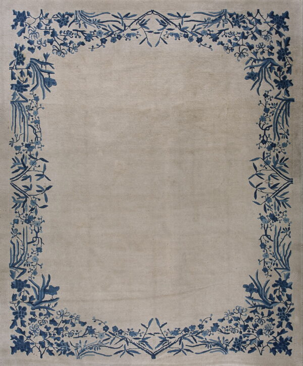 Low pile rug with a solid beige field and an elaborate blue floral and vine border.